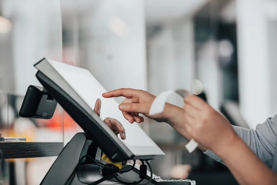 A staff member tapping a POS screen at the counter with a printed receipt